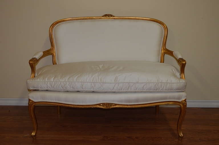 Louis XV style gilded canape with some hand carved floral details. The canape has been newly upholstered in a beautiful cream silk, with a separate seat cushion filled with dawn and feather.