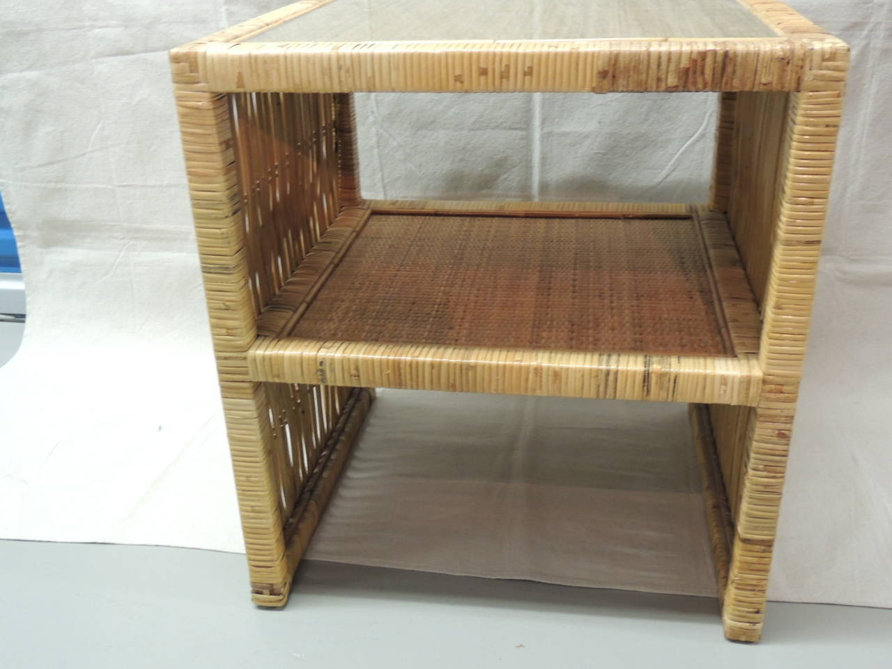 Vintage rattan and wicker square side table with clear glass inset top. Middle shelf. Basket weave deign on shelves tops.