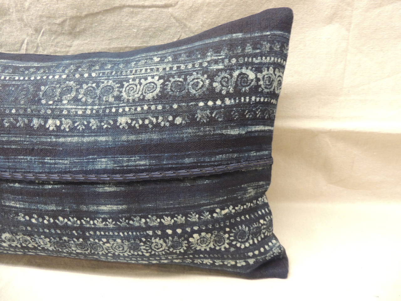 Blue and white hand-blocked batik bolster pillow with navy frame and linen backing, decorative braided detail on middle seam.