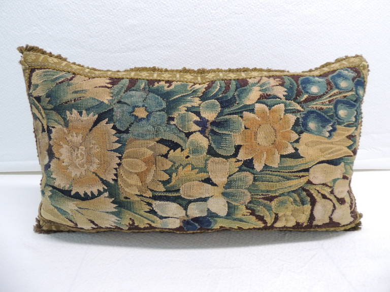Antique textile Verdure tapestry bolster pillow, tape/trim framing the pillow all around in shades of moss green, brown silk velvet backing. Tapestry depict flowers in full bloom in shades of yellow, green, soft blues on a brown background.