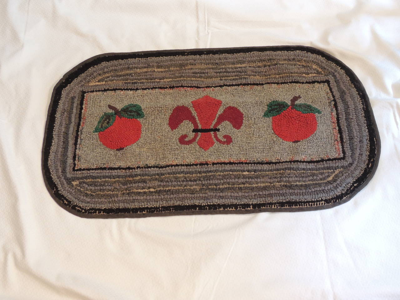 Antique Textiles Galleries...
Primitive oval hook rug, depicting fruits and Fleur-de-lis center. In shades of red, orange, green, grey and black.
Rug hooking is both an art and a craft where rugs are made by pulling loops of yarn or fabric through a
