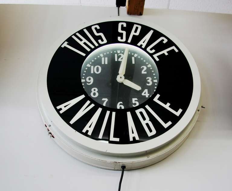 This clock was found by Chicago. Metal casing, painted white, contains a glass front, black and which saying 'This Space Available.' Neon lighting back lights this front glass panel and the face of the clock. Face is black with white letters and