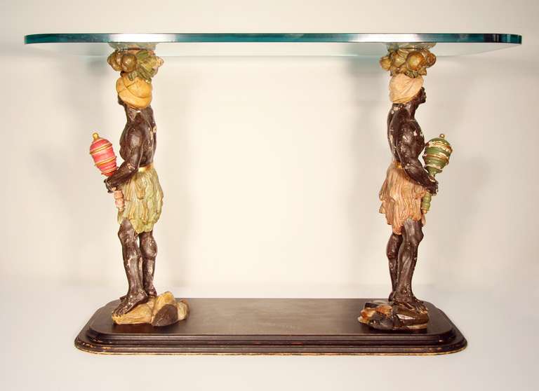 A fantastic example of blackamoor. Two hand carved and painted figures that hold up a glass top. They are mounted onto black painted bevelled wood base.
