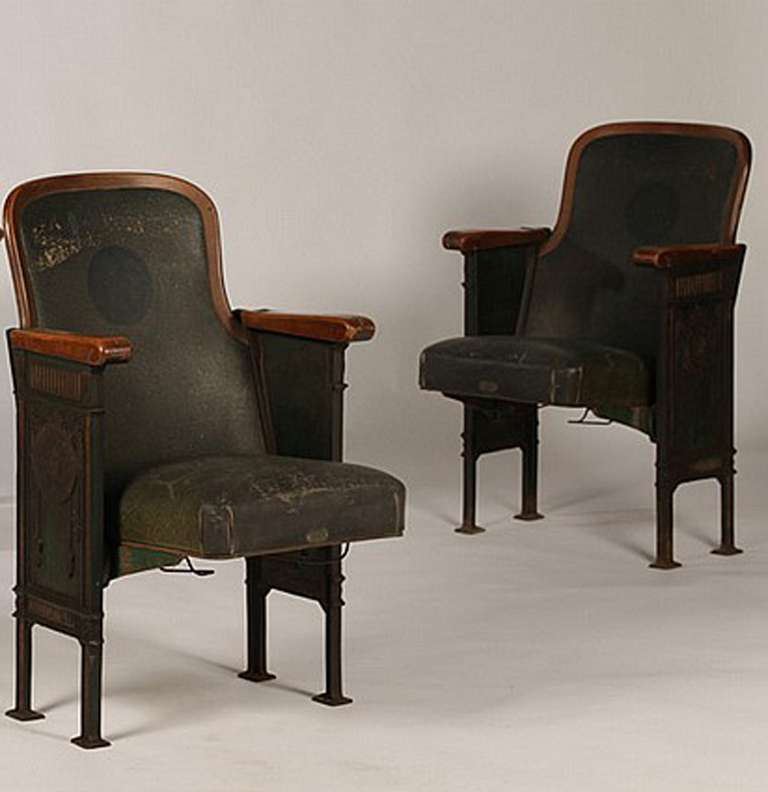 Upholstered flip down theater seats with cast iron sides. Upholstery is a dark blue with a blond wood curved back. Sides are cast with drapery and the title 