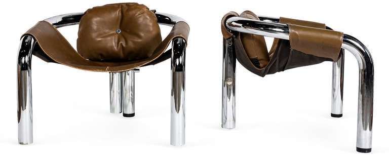 A pair of three legged chrome sling chairs.1970s. A unique set of low occasional chairs with slung leather seats and backs formed from thick chrome tubing. The back has an attached cushion with a single button tuft. Leather is in original