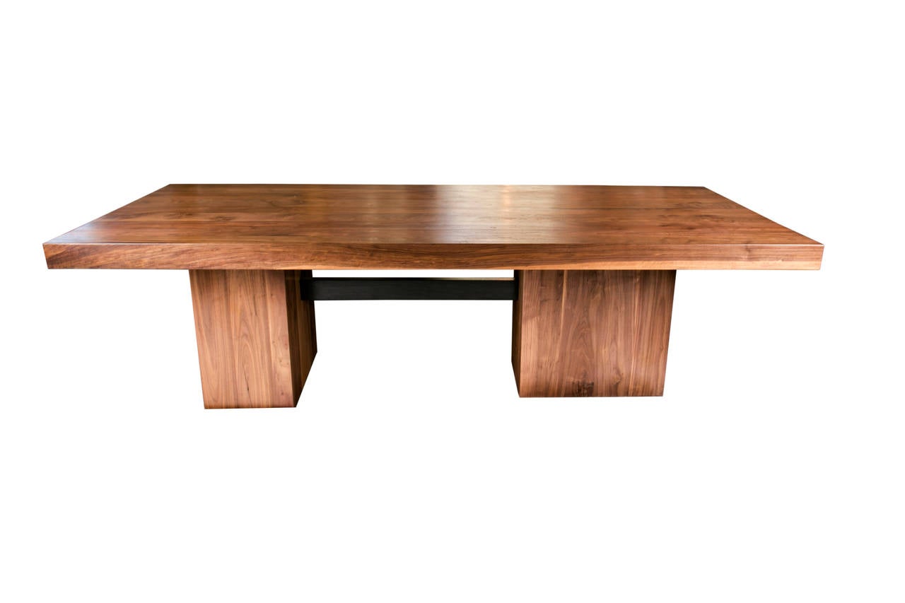 This raw but sophisticated dining table is constructed from solid slabs of kiln-dried walnut and is an updated take on the classic trestle style. The two solid walnut bases are offset at 90 degrees from one another, and are joined by an ebonized