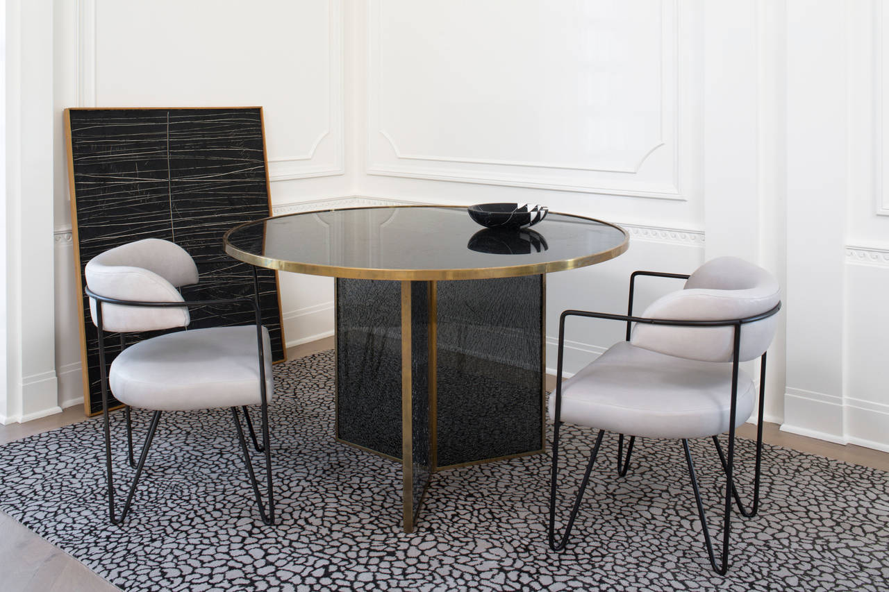 This incredibly functional and glamorous table is created by layering sheets of shattered glass between sheets of clear and smoked glass. The top and base are trimmed in solid brass with a hand rubbed patina. Light passing through the glass is