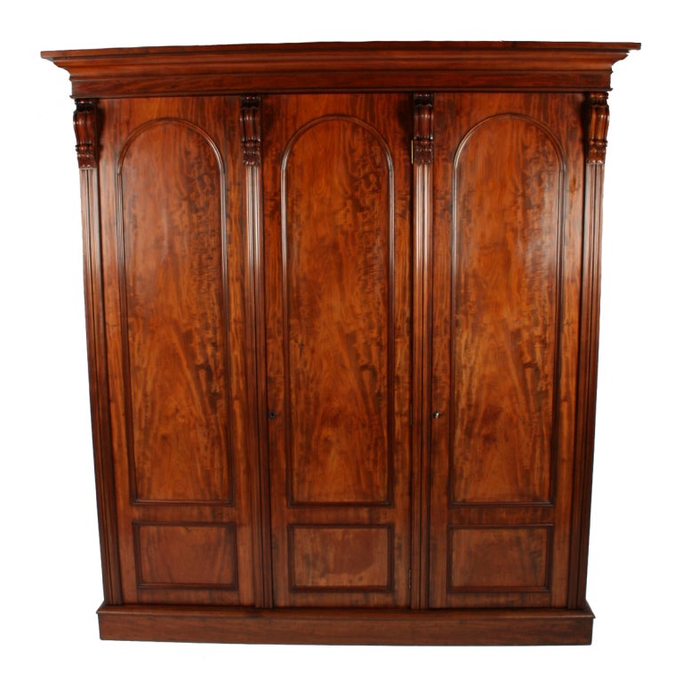 An early Victorian mahogany three door wardrobe.

The wardrobe has hanging space, interior drawers and trays and each door has two panels of figured mahogany with carved decorations at the top.

The right hand door opens to a full length hanging