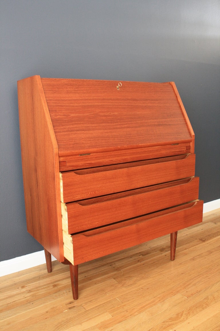 This vintage Mid-Century teak secretary has plenty of storage with  three drawers below and many storage compartments above. The drop down desk top has a key to secure it and is 28