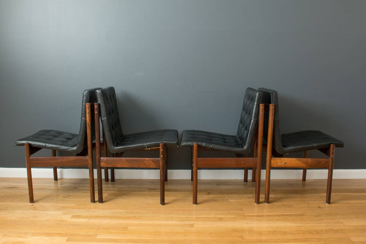 This is a set of eight vintage Mid-Century rosewood dining chairs by J.D. Moveis e Decoracoes Ltd, Sao Paulo, circa 1960's. Inconspicuous metal supports give the seats the illusion of floating over chair frames. Original black leather upholstery.