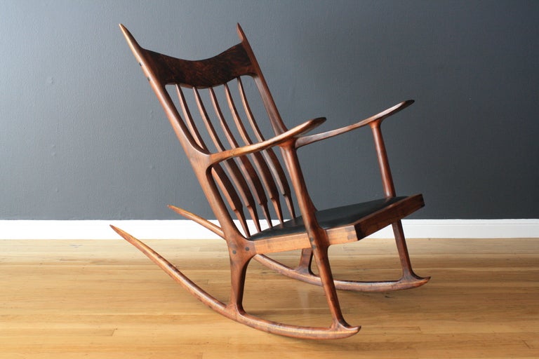 This iconic rocking chair was designed by Sam Maloof, but we believe it to have been hand crafted by a student of Maloof because is does not have the Maloof stamp. It has a Claro walnut frame with exposed doweled joinery, and a hand rubbed oil