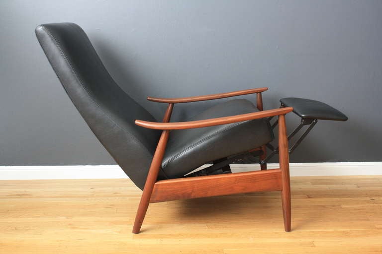 This is a vintage Mid-Century lounge chair by Milo Baughman.  It reclines back and can be used in three positions.  The foot rest comes out when reclined. This chair has a walnut frame and black faux leather upholstery.