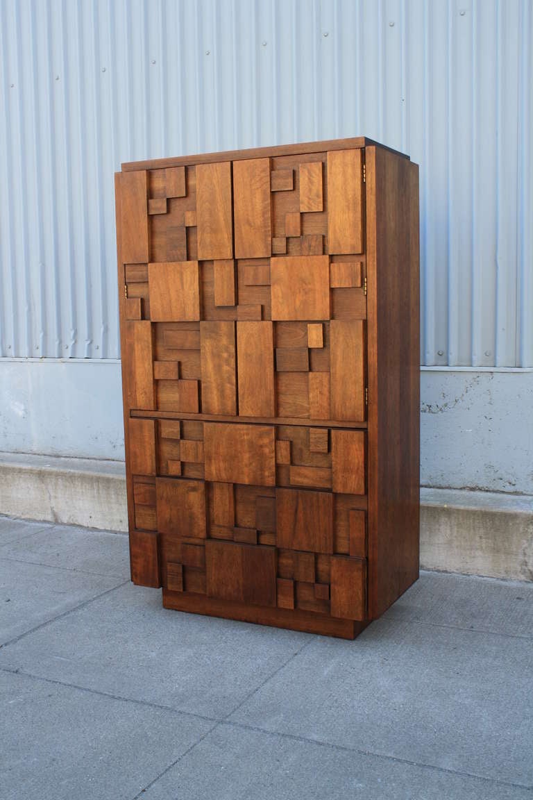 This is a Mid-Century Modern brutalist walnut dresser/chest by Lane. This tall storage piece has three drawers below and two doors above that conceal one drawer and two adjustable shelves. It is in great condition.