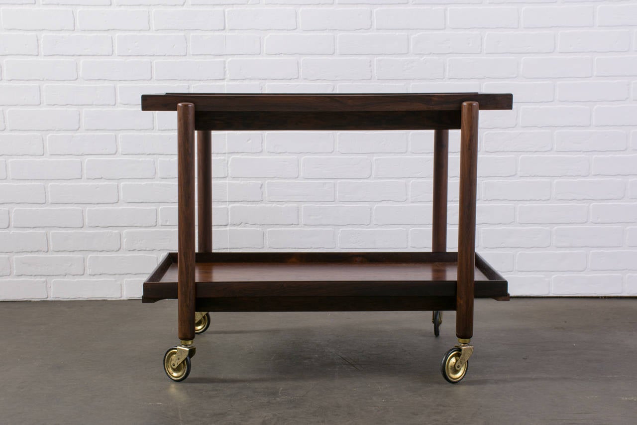 This is a vintage Mid-Century rosewood tea or bar cart by Poul Hundevad. The top tray slides over and the bottom tray can be removed to place on top. It rolls on four casters.

Measurements:
29.5-59
