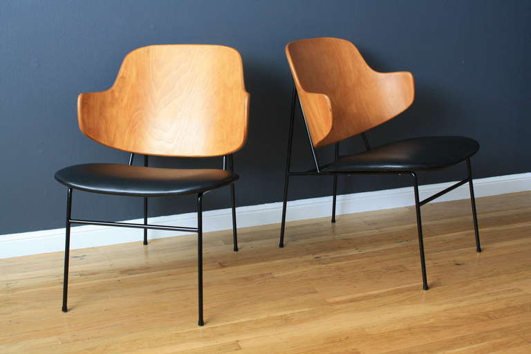 This is a pair of Mid-Century Modern penguin chairs designed by Ib Kofod Larsen. They have metal frames, bent wood backs and black leather seats.