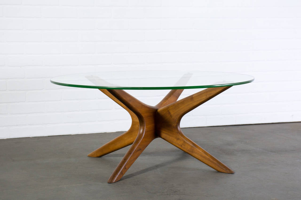 This is a Mid-Century Modern coffee table by Adrian Pearsall. It has a sculptural walnut base and a round glass top.