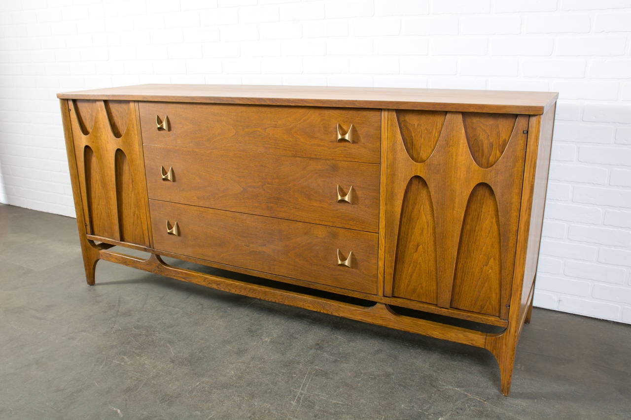 This is a vintage Mid-Century walnut sideboard by Broyhill.  It has a door on each side that conceals one shelf and three drawers in the middle. The Brasilia line is a a collection that was first presented at the World's Fair in Seattle in 1962 as a