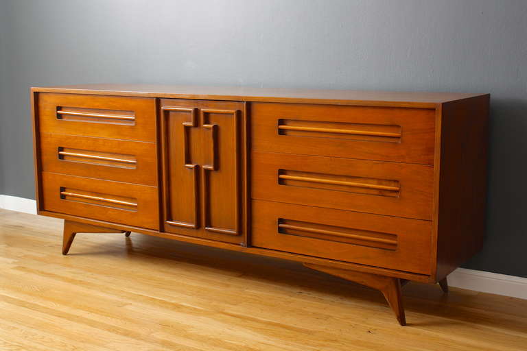 This is a vintage Mid-Century low dresser by Genova Furniture, Brooklyn, N.Y. It has three drawers on each side and a door in the middle that conceals three small drawers. Beautiful sculptural details throughout.