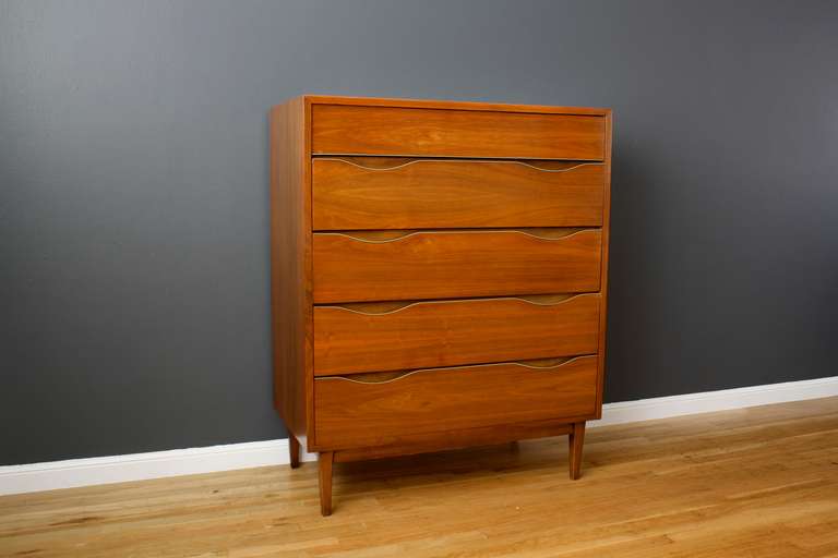 This is a vintage Mid-Century five drawer tall dresser by American of Martinsville. It is walnut with gold metal accents.