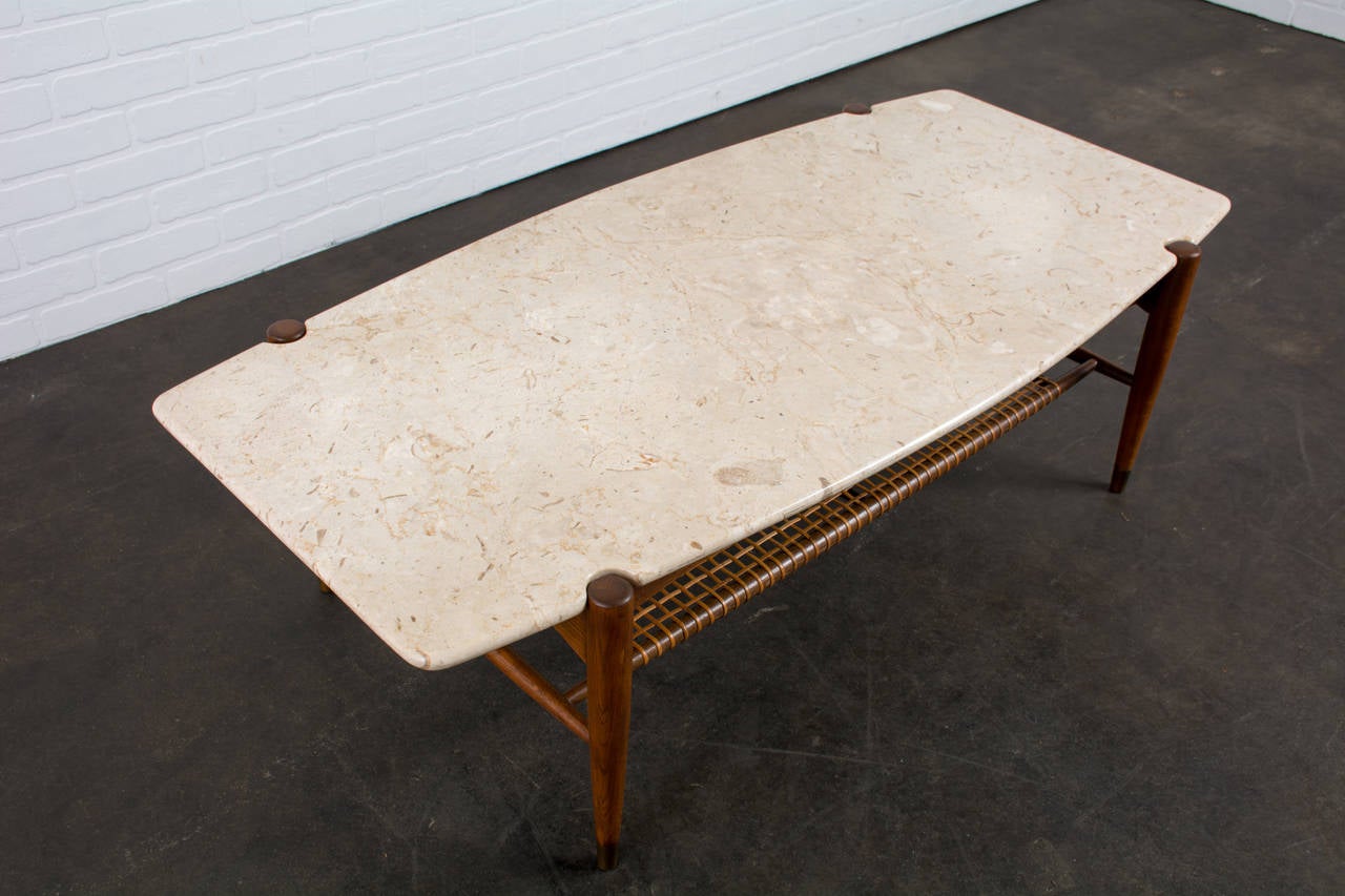 This is a Scandinavian Modern coffee table that was designed by Folke Ohlsson for Dux (Model 1305).  It features an Italian travertine top and an oak base with a cane shelf and brass caps on the legs.