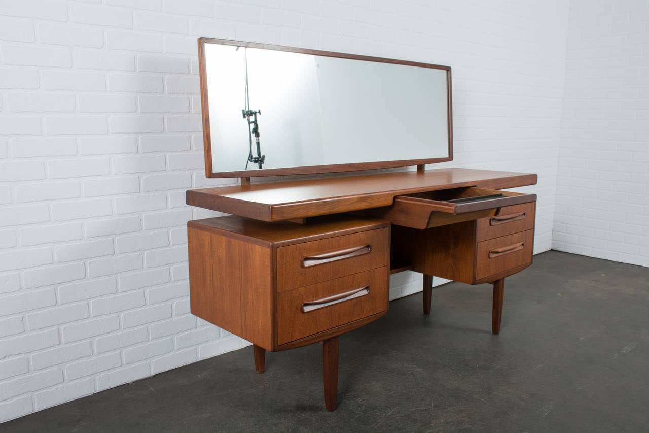 This Mid-Century Modern teak and walnut vanity/writing table was designed by Ib Kofod-Larsen for G-Plan, circa 1960s. It has a floating top, two drawers on each side and one drawer in the middle. Mirror tilts and can be removed to use as a desk (47