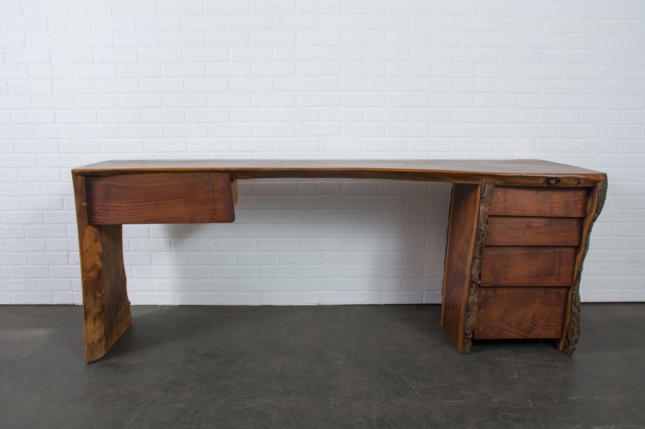 This is a vintage live edge walnut slab desk, circa 1970's. It has has four drawers on the right and one drawer on the left.