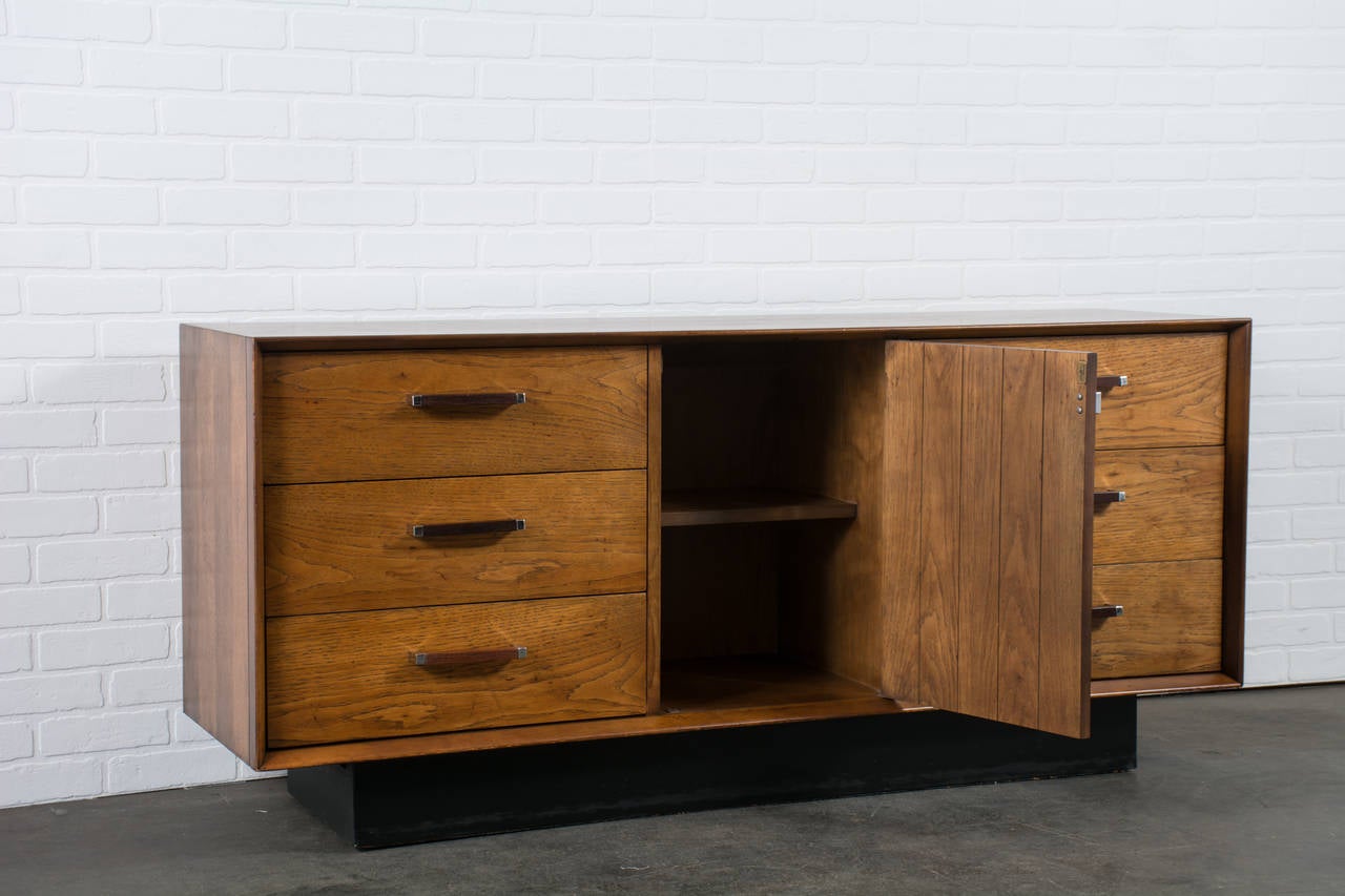 This Mid-Century Modern dresser by Lane features six drawers and one door in the middle that conceals one shelf. It is oak and rosewood with chrome and rosewood pulls.