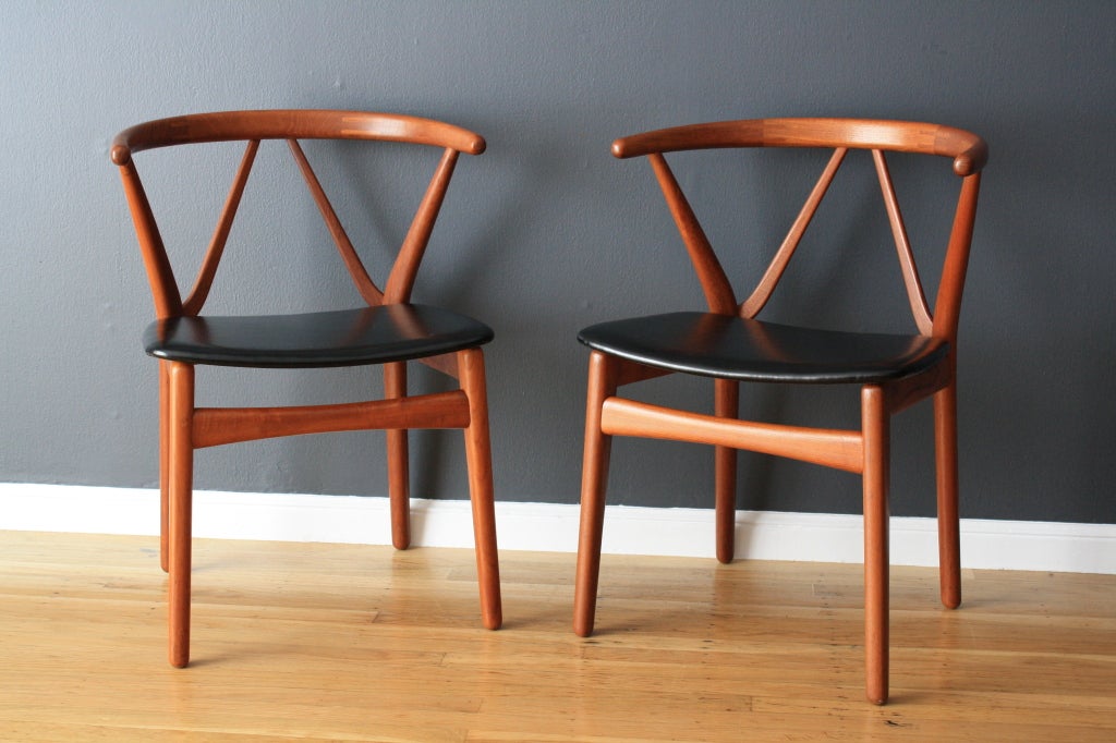 This is a pair of vintage Mid-Century teak arm chairs by Henning Kjaernulf for Bruno Hansen. They have beautiful sculptural details and black vinyl seats.