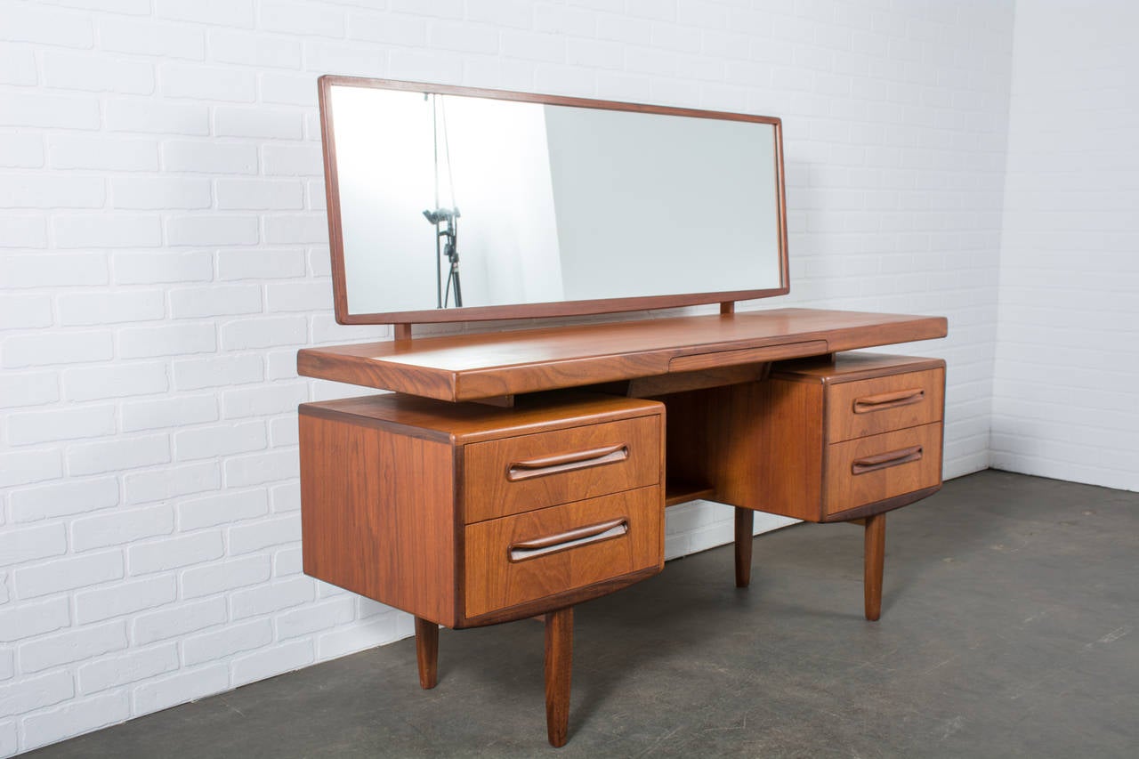 This Mid-Century Modern teak and walnut vanity or writing table was designed by Ib Kofod-Larsen for G-Plan, circa 1960s. It has a floating top, two drawers on each side and one-drawer in the middle. Mirror tilts and can be removed to use as a desk
