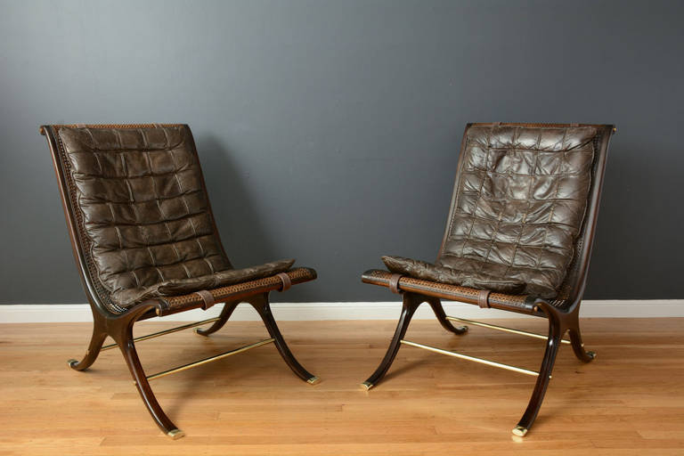 This is a pair of vintage Mid-Century lounge chairs designed by Gerald Jerome for Heritage in 1968 (Design 10). They have sculptural lines with elegant 'x' bases and caned scoop frames.  These chairs have solid brass accents and the original brown