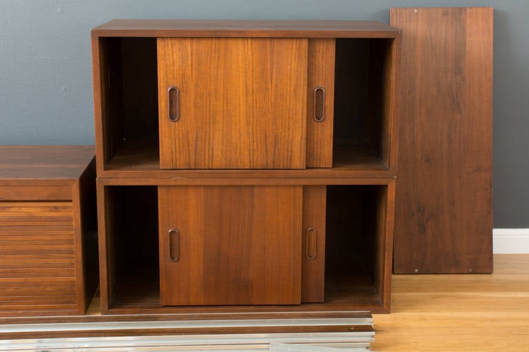 This is a Mid-Century Modern walnut OMNI wall unit by George Nelson.  It includes three boxes, two with sliding doors and one with a tambour top that slides into the top.  It also includes five shelves, four suspension poles, one lamp, and the rest