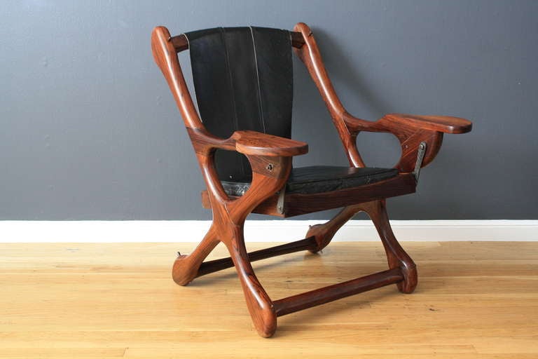 This vintage Mid-Century lounge chair by Don Shoemaker is a wonderful representation of Mexican Modernism. It features a solid wood sculptural frame and a leather sling type back rest and leather seat cushion on a wood seat. The seat hangs on