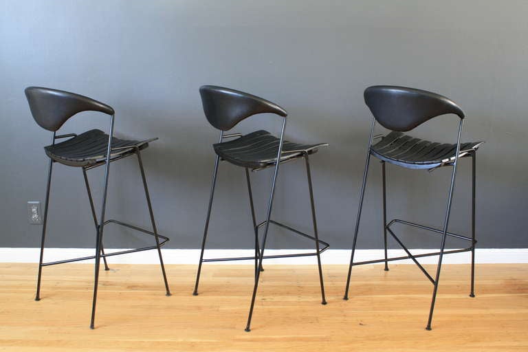 This is a set of three vintage Mid-Century bar stools designed by Arthur Umanoff in the 1950's. They have wrought iron frames and black wood slat seats.  The backrests have been professionally reupholstered in black leather.