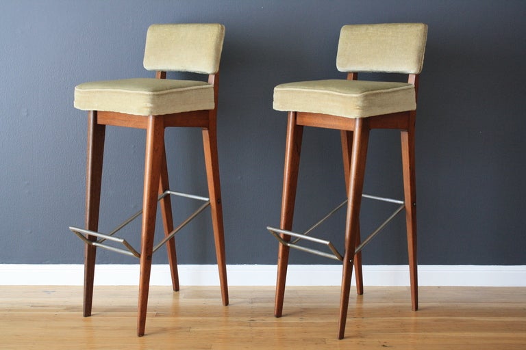 This is a pair of vintage Mid-Century teak bar stools with metal foot rests.  The original upholstery is in great condition with minor vintage wear.