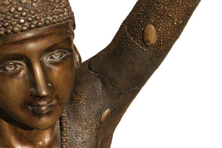 This Art Deco style statue after Demetre Chiparus is skillfully rendered in bronze. The near five foot dancer stands poised with raised arms in a full length beaded leotard. The statue is mounted on a circular bronze base.