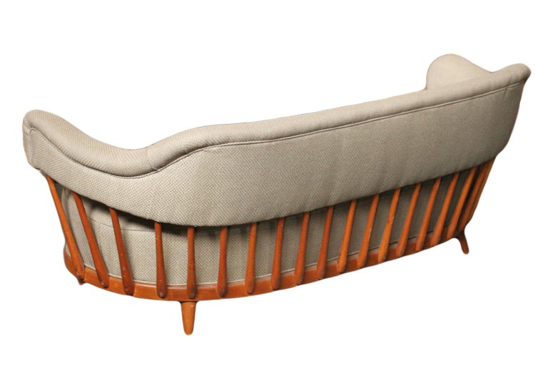 This mid-century modern sofa features an elegant spindle frame which wraps around the sides and supports the tufted back rest. The cloud-shaped sofa retains its original upholstery and rests on tapered legs.