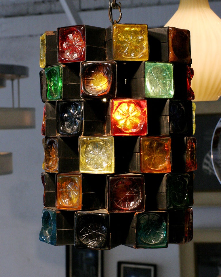 This cheerful 1960s pendant lamp from  features a stacked, cylindrical iron frame inset with hand blown glass squares. Each glass piece is embossed with a floral or veined leaf motif; they come in a range of colors including teal, red, amber, green,