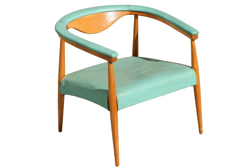 These Mid-Century Modern barrel back armchairs feature the original teal vinyl upholstered seat and backrest that winds all the way around the circumference to cover the armrests. The chairs' frame, including the demilune back rests, are rendered in