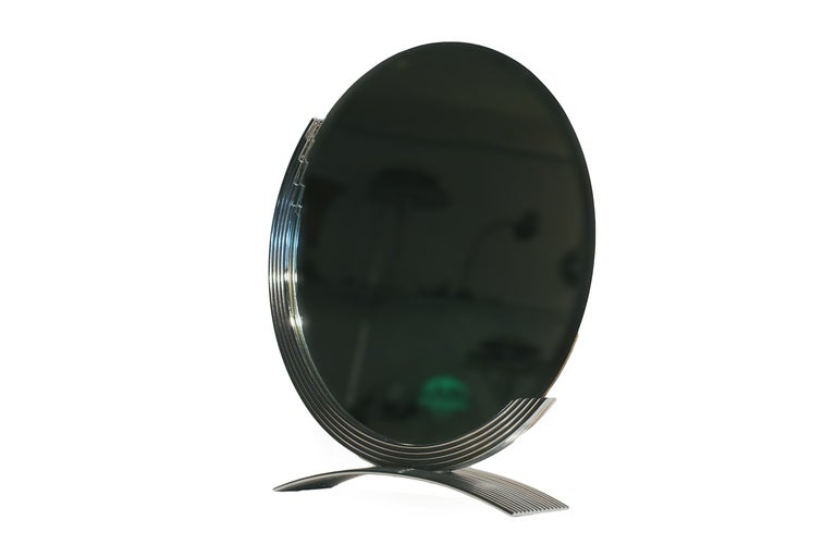 This elegant Art Deco round table-top mirror features a demilune frame which rests on an arched base both of which are in chrome. The beveled mirror was rechromed and remirrored with care in Los Angeles in the 1970s.

Please inquire us if you