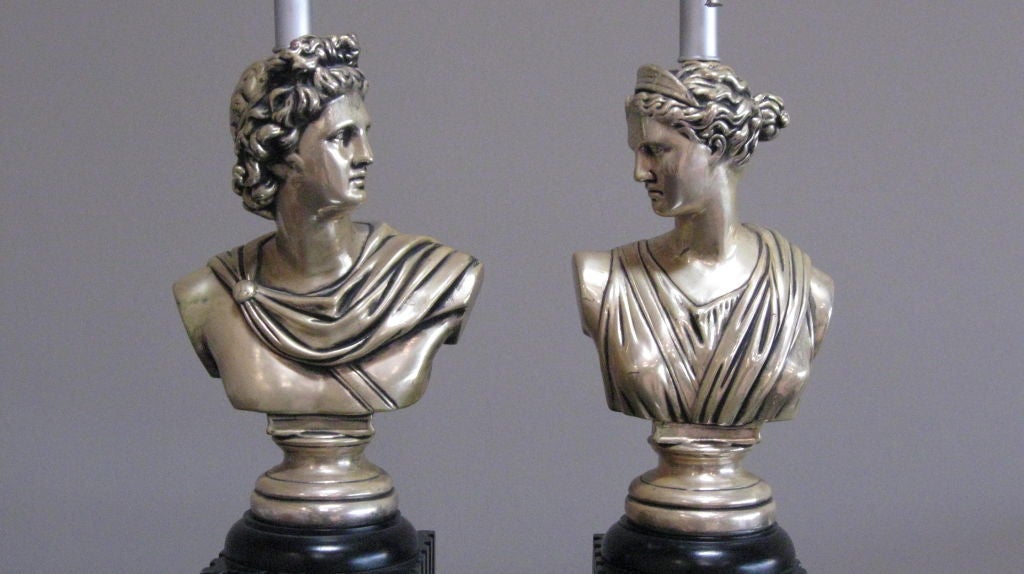 Cette paire de lampes de table de style néoclassique des années 1950 présente des bustes de dieux grecs montés sur la moitié inférieure d'une colonne dorique laquée. Les personnages sont habilement sculptés dans le bois et finis avec une riche laque