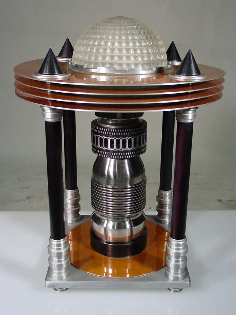 In what can only be described as retro futurism, this stunning Art Deco Machine Age Table Lamp features a domed glass waffle shade surrounded by four copper colored rings, all of which are held in place by four dramatic aluminum poles. It's a Deco
