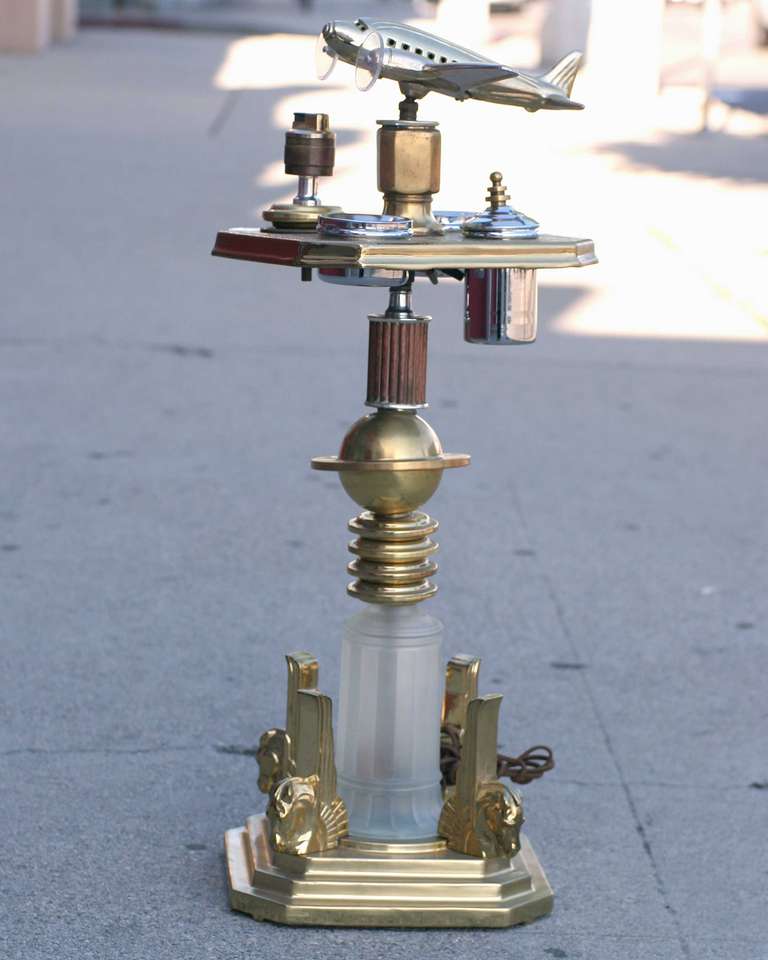 Brass Art Deco ashtray stand featuring a decorative light up airplane on top with a glass light up bass on the bottom. 

The stand comes with a built in light, 2 ashtrays and Tobacco canister.