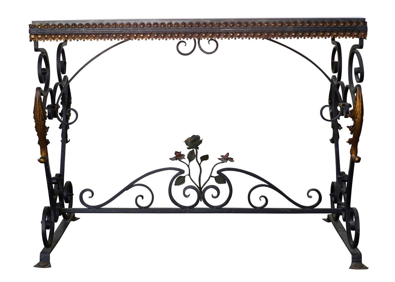 Late Victorian Wrought Iron Console Table with Italian St Laurent Marble Top. The table features an iron floral sculpture along the center rail and gold tone accents along the legs and table top. The Scrolling rails come together to make a beautiful