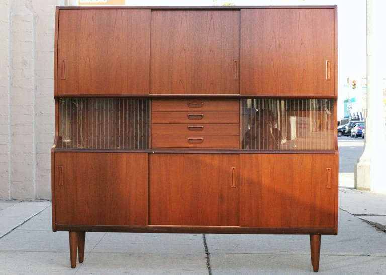 Danish Modern Walnut Hutch with a center mirrored bar, an assorted of six drawers, 5 shelf storage blocks and two display cases with sliding glass doors. 

Very high quality all original cabinet with subtle modernist dark stained walnut front in
