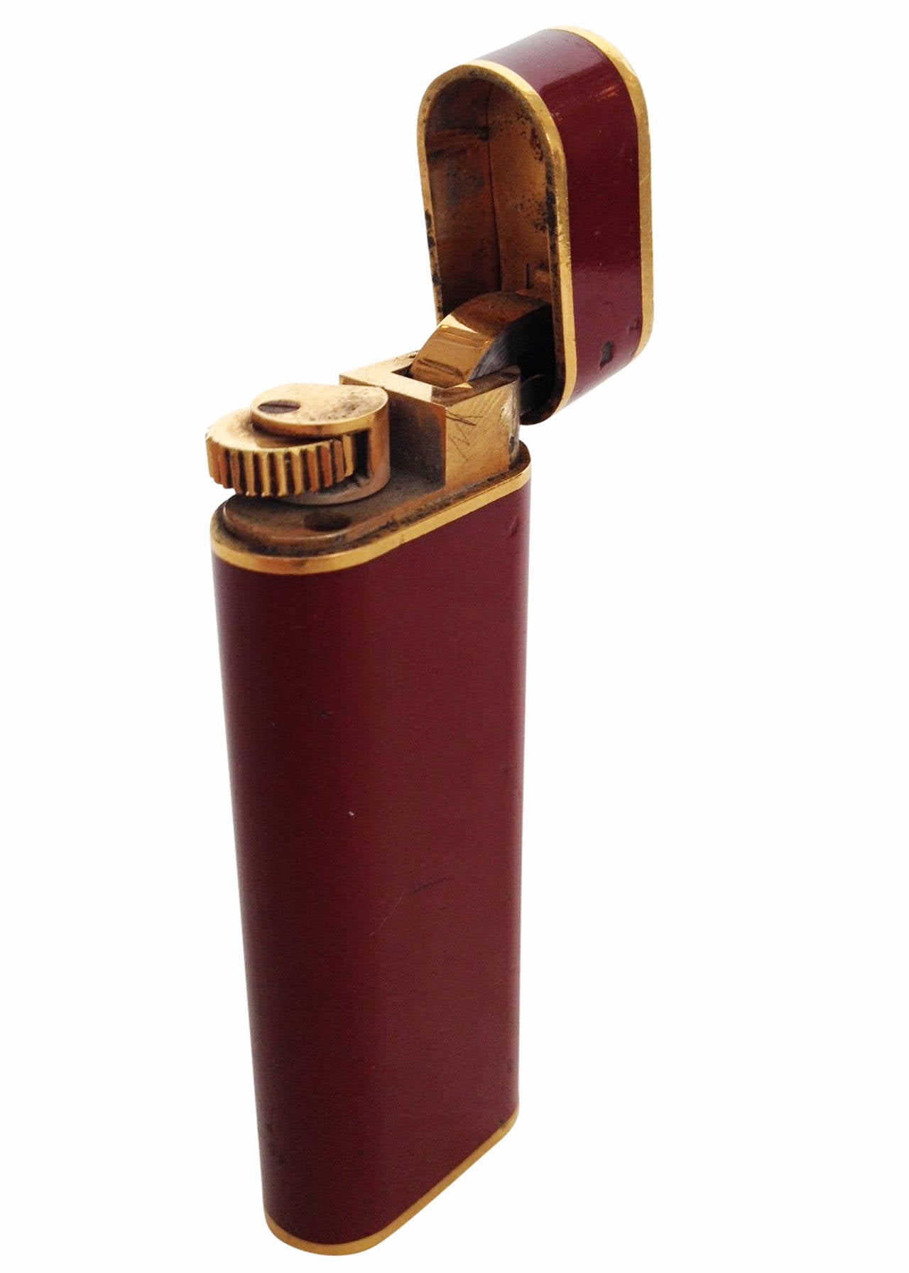 Made by Cartier, this 18-karat gold plated and black enamel lighter features an oval body with a beautiful, burgundy enamel inlay with gold border. Also feature is an interlocking 