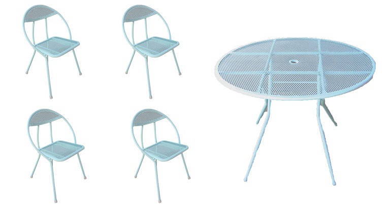 This mid-century modern outdoor dining set by Salterini features four rounded-back, folding chairs and a circular dining table with a hole in the center for an umbrella. The table and chairs are made of a combination of mesh and tubular steel all