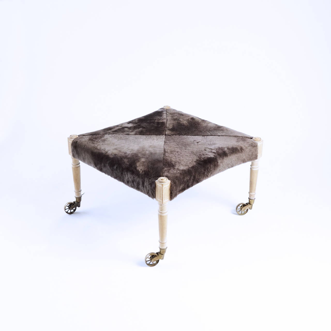 A piece whose design and proportions suggest great flexibility of use. The slender, limed wood legs end in large pivoting brass wheels. The seat is covered in a decadently soft wool shearling.