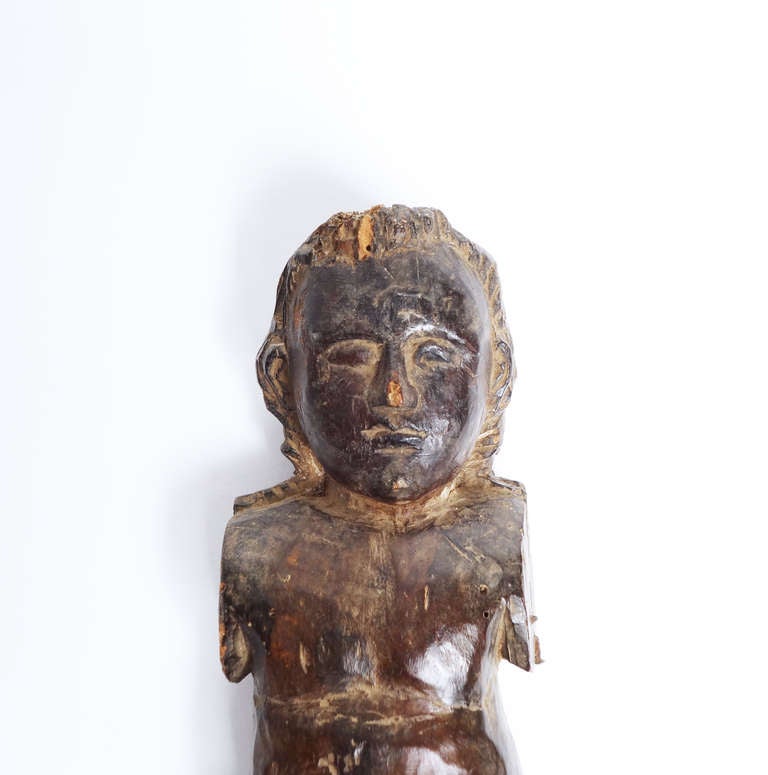 A carved, round-bellied figure of a child, one leg bent. Both arms and part of the right leg are missing. The surface has a warm, dark patina.