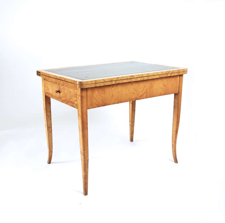 An elegant Biedermeier games table. The birch veneer is beautifully figured and well-preserved, providing the primary ornamentation on this clean-lined piece. The legs taper and turn out toward the feet, lending the design a balletic grace. The