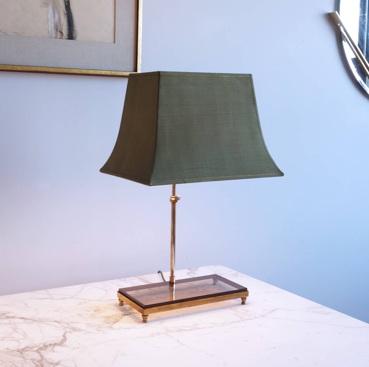 Wearing their original green silk bell shades, this pair of table lamps has a quiet and stately beauty. The slender stems are set in a smoky acrylic rectangle which rests in a bronze frame with four ball feet.

16